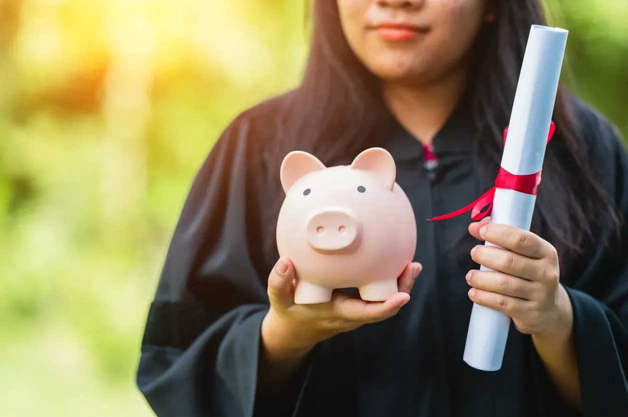 College graduate holding a diploma and a piggy bank